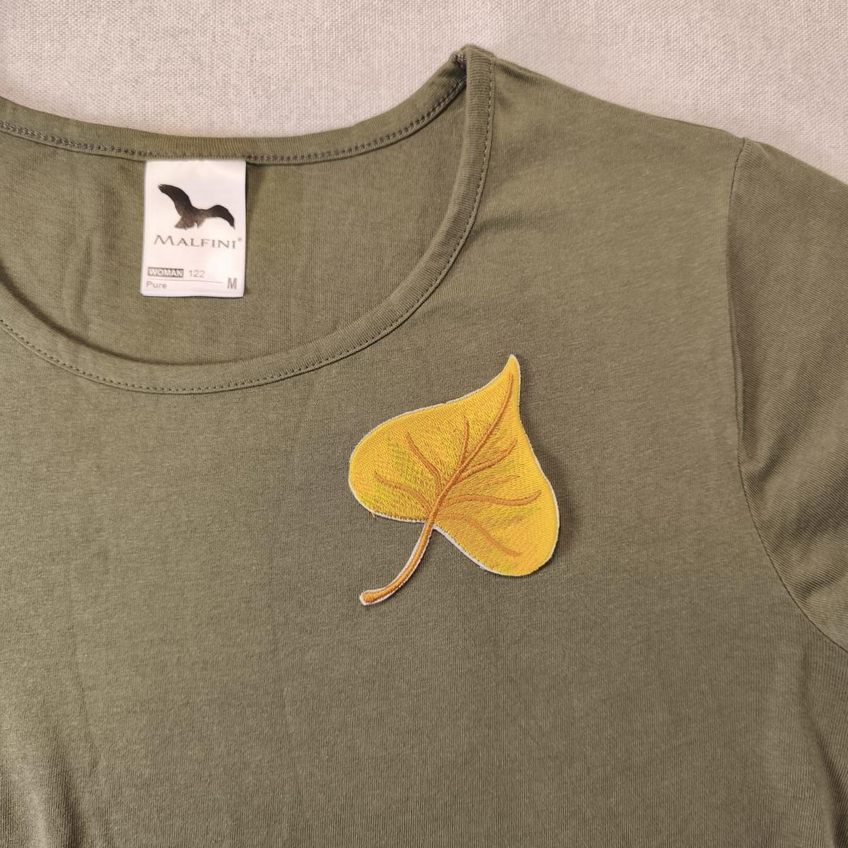 Ein Pappel Blatt Aufnäher zum aufbügeln auf einem olivgrünem T-Shirt als Beispiel auf einem neutralen Hintergrund