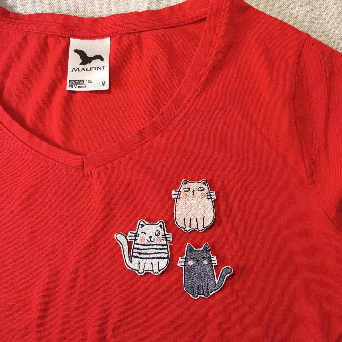 Eine Beispielaufnahme von drei verschiedenen Katzen-Aufnäher auf einem roten T-Shirt.